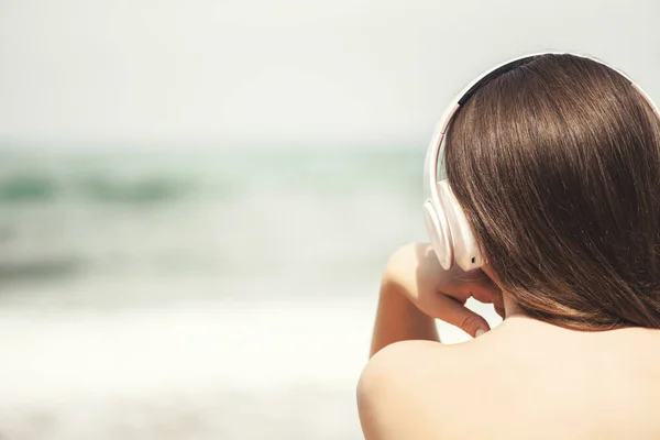 一个女人坐在海滩上 戴着耳机 听着音乐 梦想着大海 暑假期间的女性放松 — 图库照片