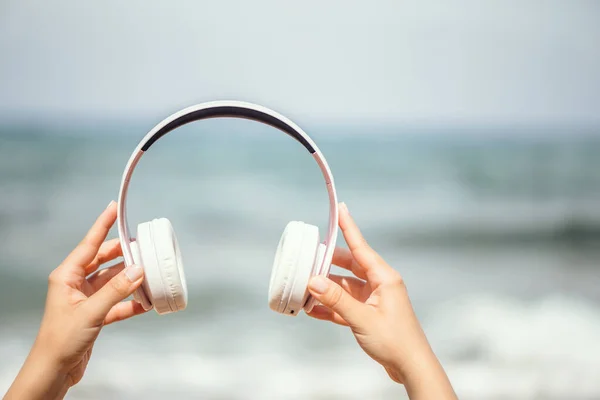 Woman hands with headphones on a beach and sea coastline.