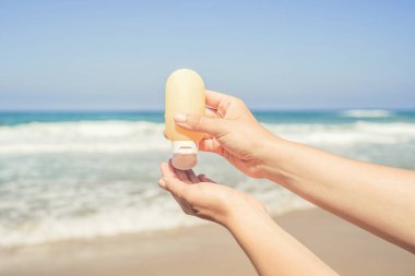 Deniz kıyısındaki bir sahilde el kremi süren bir kadın. Yaz tatilinde kadın dinlenmesi. Arka plan