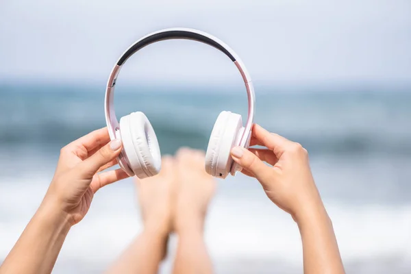 Woman hands with headphones on a beach and sea coastline.