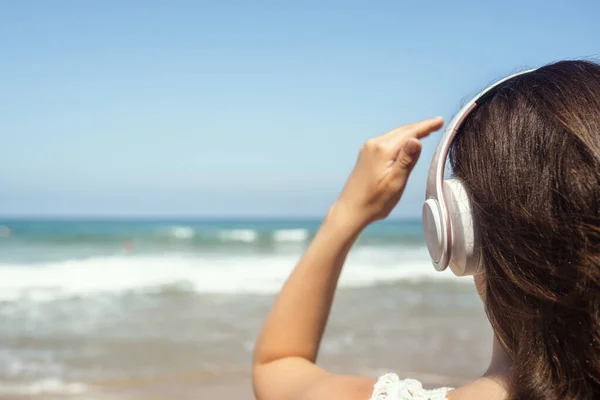 Alone woman on a beach in headphones listen music looking on the sea. Female relaxation at summer vacation. Back view