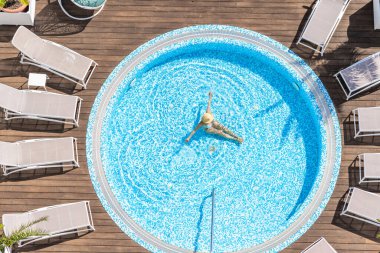 Yalnız, bikinili ve şapkalı güzel bayan jakuzide, tahta terasta yüzüyor. Yukarıdan insansız hava aracı görüntüsü. Tropik yaz lüks oteli