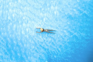 Yalnız, bikinili ve şapkalı güzel bayan yüzme havuzunda yüzüyor. Yukarıdan insansız hava aracı görüntüsü. Tropik yaz tatili