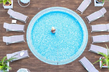 Yalnız, bikinili ve şapkalı güzel bayan jakuzide, tahta terasta yüzüyor. Yukarıdan insansız hava aracı görüntüsü. Tropik yaz lüks oteli