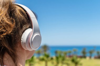 Plajda kulaklıklarıyla yalnız bir kadın denize ve palmiye ağaçlarına bakarak müzik dinliyor. Yaz tatilinde kadın dinlenmesi. Arka plan