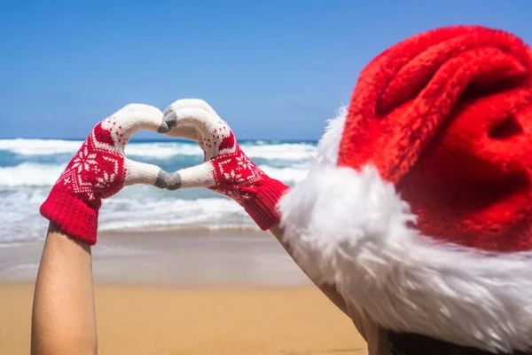 クリスマス海の休日 サンタの帽子と手袋の幸せな女性のバックビューは 手から心臓の形を示し 楽園のビーチアイランドの休暇にリラックスしてください — ストック写真