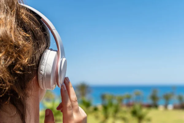 Alone woman on a beach in headphones listen music looking on the sea and palm trees. Female relaxation at summer vacation. Back view