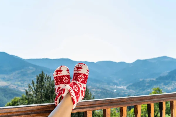 Woman in Christmas red socks, boots sits on a balcony in the mountains