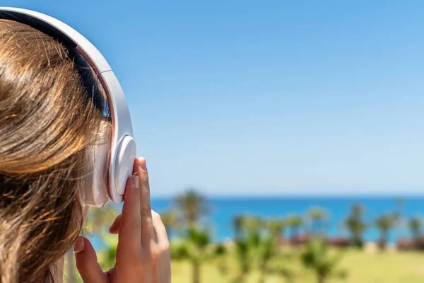 Alone woman on a beach in headphones listen music looking on the sea and palm trees. Female relaxation at summer vacation. Back view