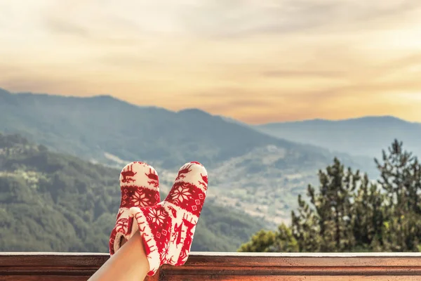 Woman in Christmas red socks, boots sits on a balcony in the mountains at sunset