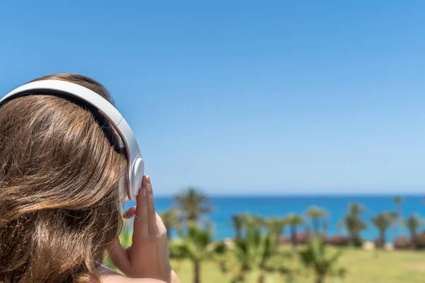 一个人坐在海滩上 戴着耳机 听着音乐 望着大海和棕榈树 暑假时的女性放松 背景色 — 图库照片