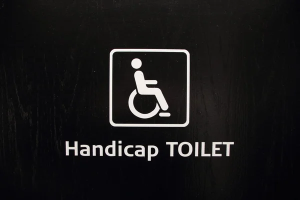 Weißes Behindertentoilettenschild auf schwarzem Holz — Stockfoto