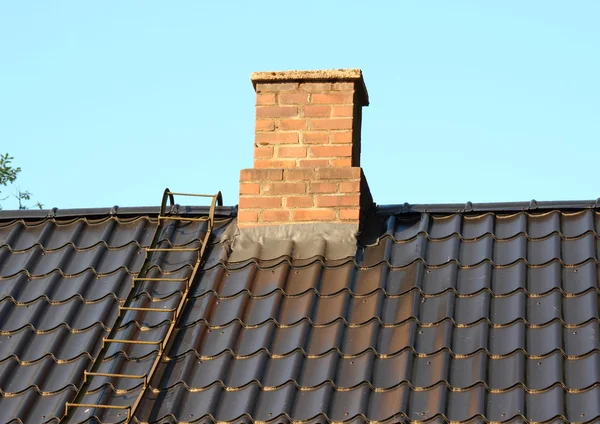 Brick chimney on black roof with metal ladder — Stock Photo, Image