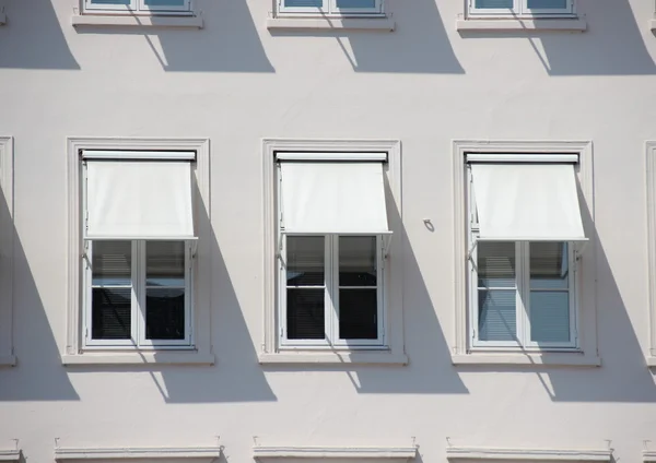 Drei Fenster auf grauem Gebäude mit weißen Markisen und Schatten — Stockfoto