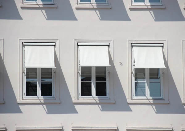 Drie ramen op grijs gebouw met witte zonweringen en schaduw Rechtenvrije Stockafbeeldingen