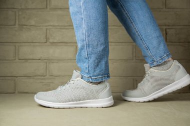 Kot pantolon ve spor ayakkabı giyen genç moda kadını bacakları. Bir kız tuğla duvarın önünde yürüyor
