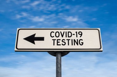 COVID-19 test levhası, mavi gökyüzü arka planında ok. Kopya alanı olan tek yönlü boş yol işareti. Bir direğin üzerindeki ok tek yönü gösteriyor..