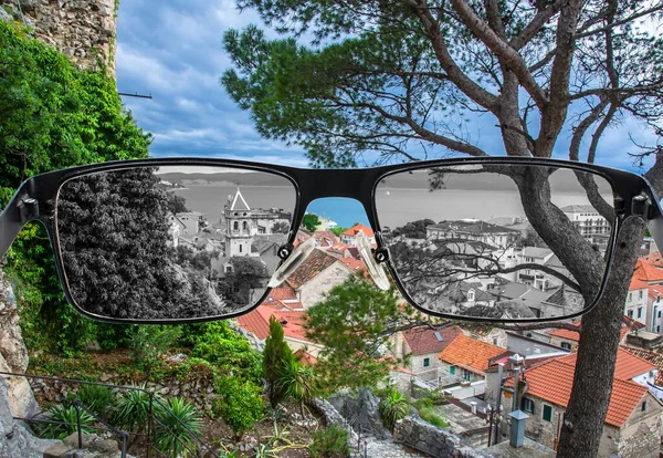 Looking through glasses to desaturated view of pine tree,  old city center with rooftops and see. Color blindness. World perception during depression. Medical condition. Health and disease concept.