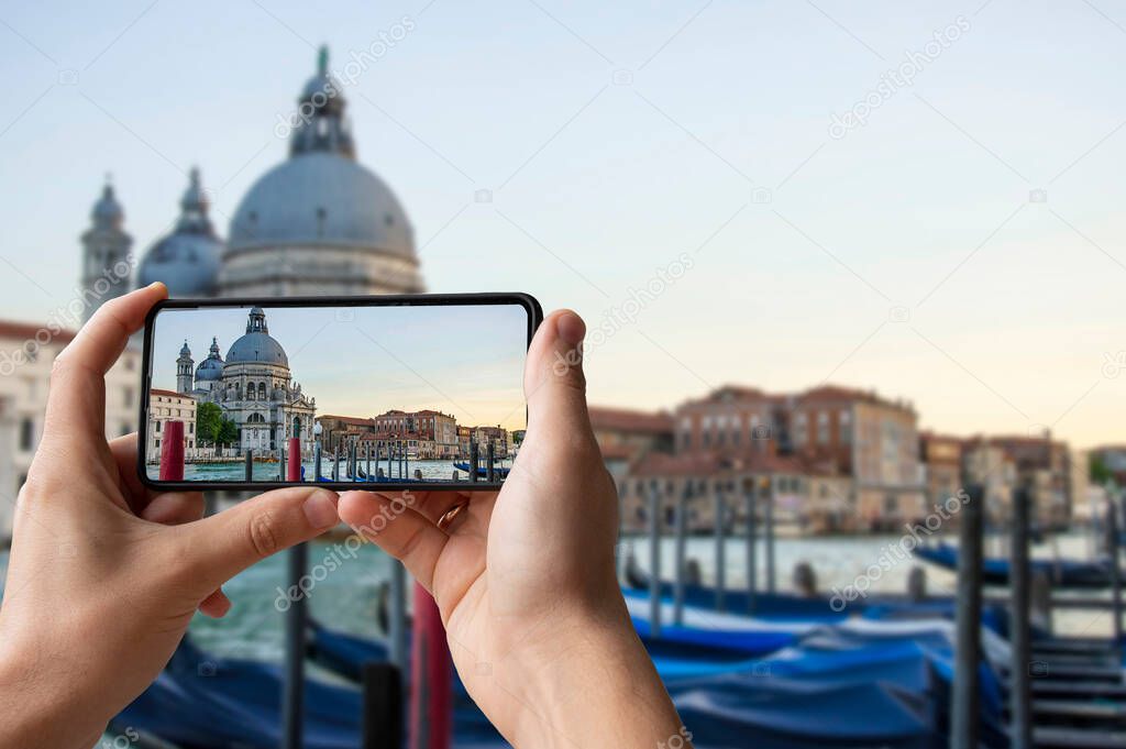 Tourist taking photo of traditional gondolas on famous Grande Canal with historic Basilica di Santa Maria della Salute in the background in Venice, Italy