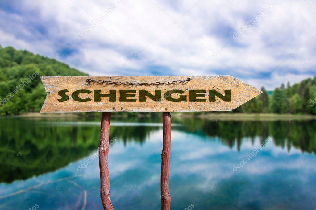 Schengen wooden arrow road sign against lake and forest background. Schengen  - European border control-free travel area