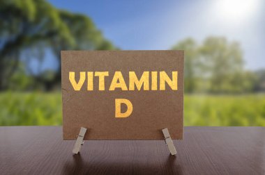 Masada üzerinde güneşli yeşil park arkaplanı olan D vitamini metni.