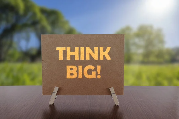 Think big text on card on the table with sunny green park background.