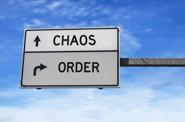 Kargaşa ve düzen içeren yol tabelası. Mavi gökyüzü arka planında metal direkli beyaz iki sokak işareti.