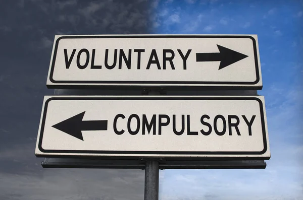 Voluntary versus compulsory road sign with two arrows on blue and grey sky background. White two street sign with arrows on metal pole. Two way road sign with text.