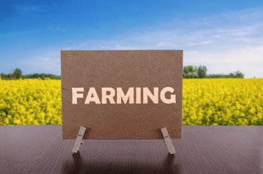 Masanın üzerinde sarı tarla ve mavi gökyüzü arkaplanı olan kart üzerinde tarım metni.