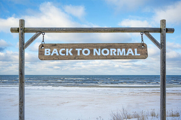 Wooden sign with text back to normal against blue sky, sea and beach with white sand. Travel and vacation concept.