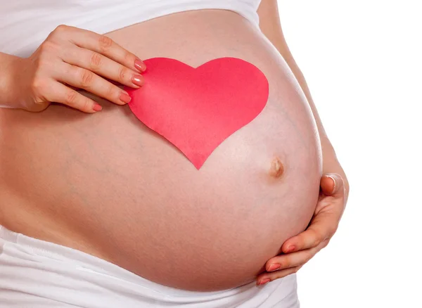 Беременная женщина держит руку на животе и держит красное сердце — стоковое фото