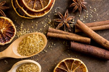 Baharatlar ve bitkiler. Yiyecek ve mutfak malzemeleri. Tarçın çubukları, anason yıldızları, esmer şeker, dokulu arkaplanda portakallar..