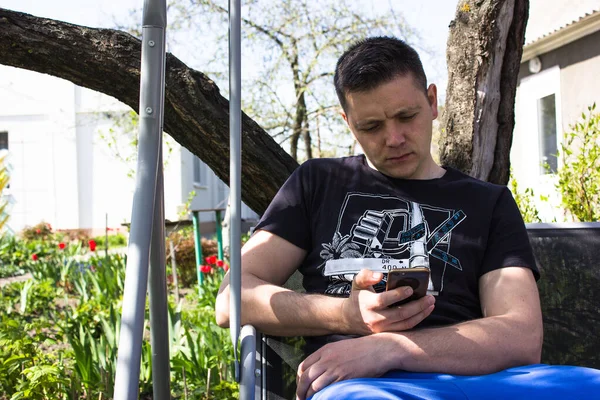 Young Sad Guy Looks Phone Swing Garden Guy Writing Message — Fotografia de Stock