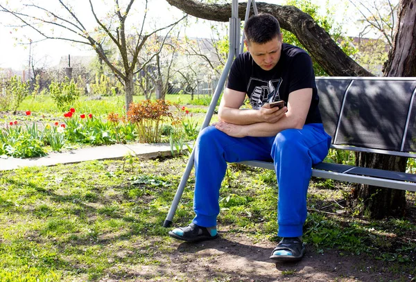 Young Sad Guy Looks Phone Swing Garden Guy Writing Message — Fotografia de Stock