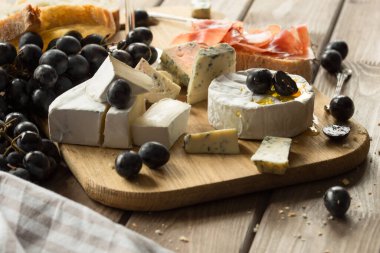 Tahta tahtada çeşitli peynirler. Camembert peyniri, küflü peynir, gouda, sert peynir, çilek, nane yaprağı, peynir için bıçak.