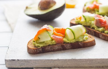 Hafif arka planda avokado ve somonlu sandviç, yeşil soğan ve glütensiz tahıl ekmeği, turp ve salatalık. konsept diyet yemekleri, fotokopi alanı, sandviç servisi, sağlıklı fast food.