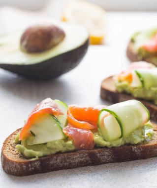 Hafif arka planda avokado ve somonlu sandviç, yeşil soğan ve glütensiz tahıl ekmeği, turp ve salatalık. konsept diyet yemekleri, fotokopi alanı, sandviç servisi, sağlıklı fast food.