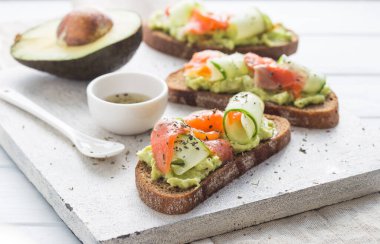 Hafif arka planda avokado ve somonlu sandviç, yeşil soğan ve glütensiz tahıl ekmeği, turp ve salatalık. konsept diyet yemekleri, fotokopi alanı, sandviç servisi, sağlıklı fast food.