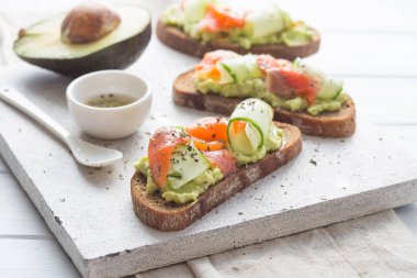 Hafif arka planda avokado ve somonlu sandviç, yeşil soğan ve glütensiz tahıl ekmeği, turp ve salatalık. konsept diyet yemekleri, fotokopi alanı, sandviç servisi, sağlıklı fast food.