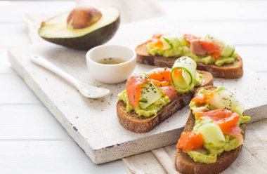 Hafif arka planda avokado ve somonlu sandviç, yeşil soğan ve glütensiz tahıl ekmeği, turp ve salatalık. konsept diyet yemekleri, fotokopi alanı, sandviç servisi, sağlıklı fast food.