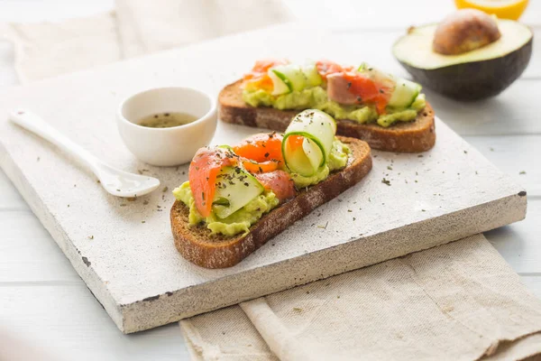 Hafif arka planda avokado ve somonlu sandviç, yeşil soğan ve glütensiz tahıl ekmeği, turp ve salatalık. konsept diyet yemekleri, fotokopi alanı, sandviç servisi, sağlıklı fast food.