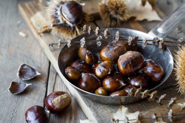 Kavrulmuş ve taze kestaneler dökme demir ızgara tavasında, ahşap tahtanın üzerinde.