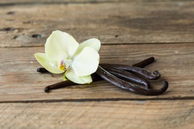 Kurutulmuş vanilya kabukları ve orkide vanilya çiçekleri ahşap arka planda