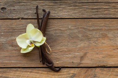 Kurutulmuş vanilya kabukları ve orkide vanilya çiçekleri ahşap arka planda