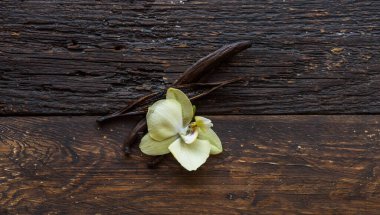 Kurutulmuş vanilya kabukları ve orkide vanilya çiçekleri ahşap arka planda