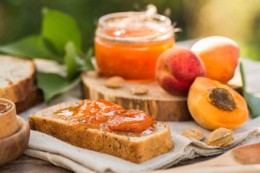 Cam kavanozda kayısı reçeli ve ahşap masada taze kayısılar.