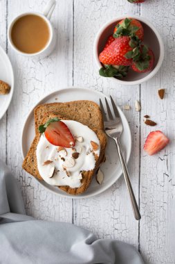 Krem peynirli tost ekmeği, çilek, badem ve eski ahşap masada kahve. Bahar yemeği konsepti. Kırsal kahvaltı, natürmort..