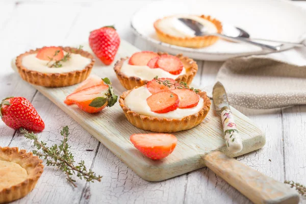 Fruit tarts, small shortcrust tarts with the addition of cream cheese, fresh strawberries and thyme on white table.