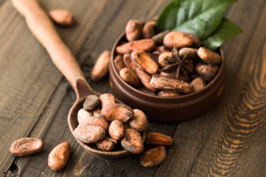 fresh organic cocoa beans in a bowl on a wooden background.
