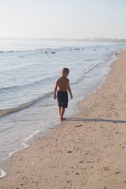 happy little kid boy running on the beach of sea. Funny cute child, making vacations and enjoying summer day